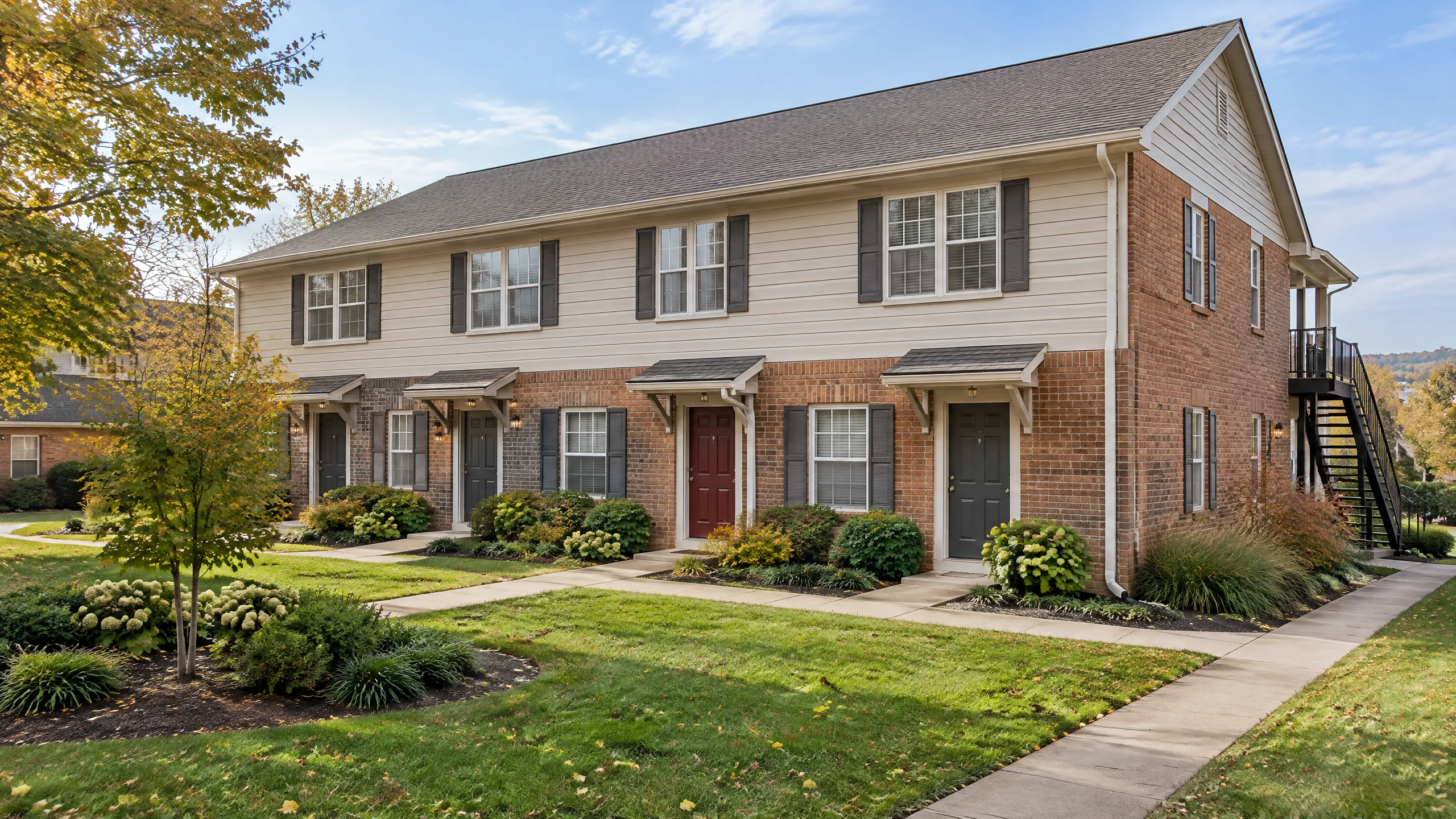 AI-generated representative two-story brick and siding multifamily building with separate entry doors, shared walkways, gutters, and an exterior stairway.
